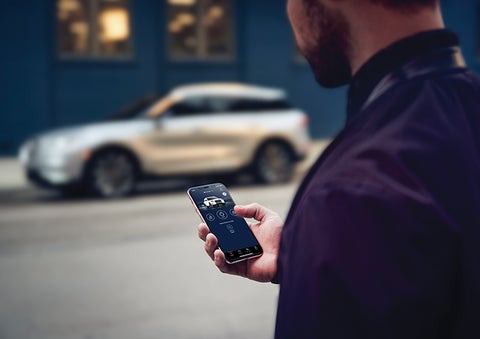 A person is shown interacting with a smartphone to connect to a Lincoln vehicle across the street. | Koons Lincoln of Bethesda in Silver Spring MD